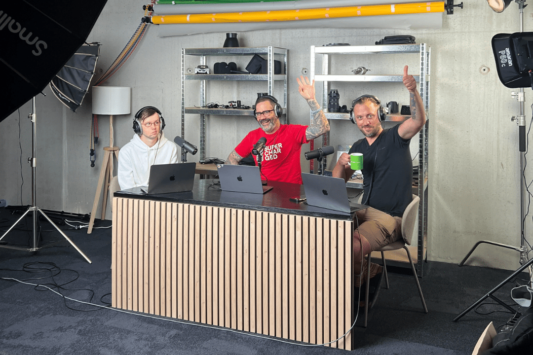 Trois journalistes de l'équipe Automobile Propre assis à une table de podcast dans un studio d'enregistrement font signe de la main à la caméra