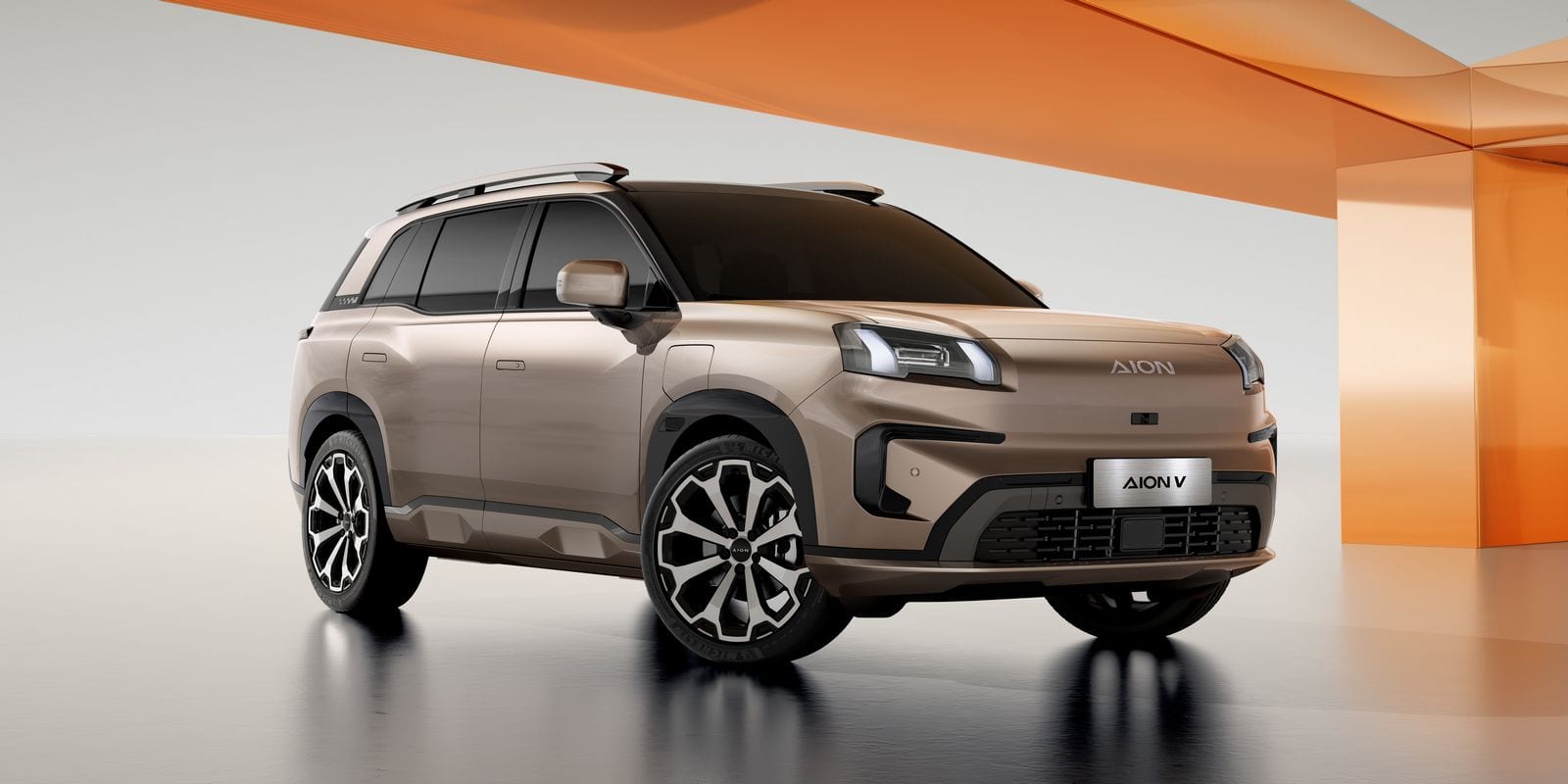 Aion V, SUV électrique beige doré, vu de trois-quarts avant en studio sur fond orange