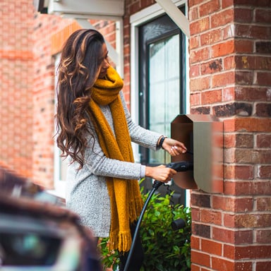 Femme branchant sa voiture électrique sur une borne de recharge murale installée sur une maison individuelle
