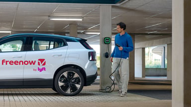 Chauffeur branchant un taxi électrique Volvo EX30 Freenow sur une borne de recharge dans un parking.