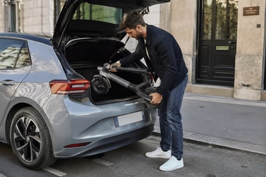 Un homme sort une trottinette électrique pliée dans le coffre d'une voiture électrique en ville