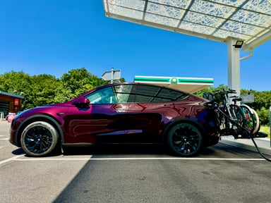 Tesla Model Y rouge équipée de vélos en cours de recharge à une borne sur la route des vacances.
