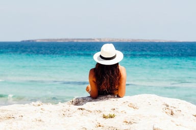 Jeune fille de dos contemplant la mer sur une belle plage déserte de sable blanc