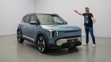 Kia EV2 bleu, vue trois-quarts avant avec personne debout à côté.