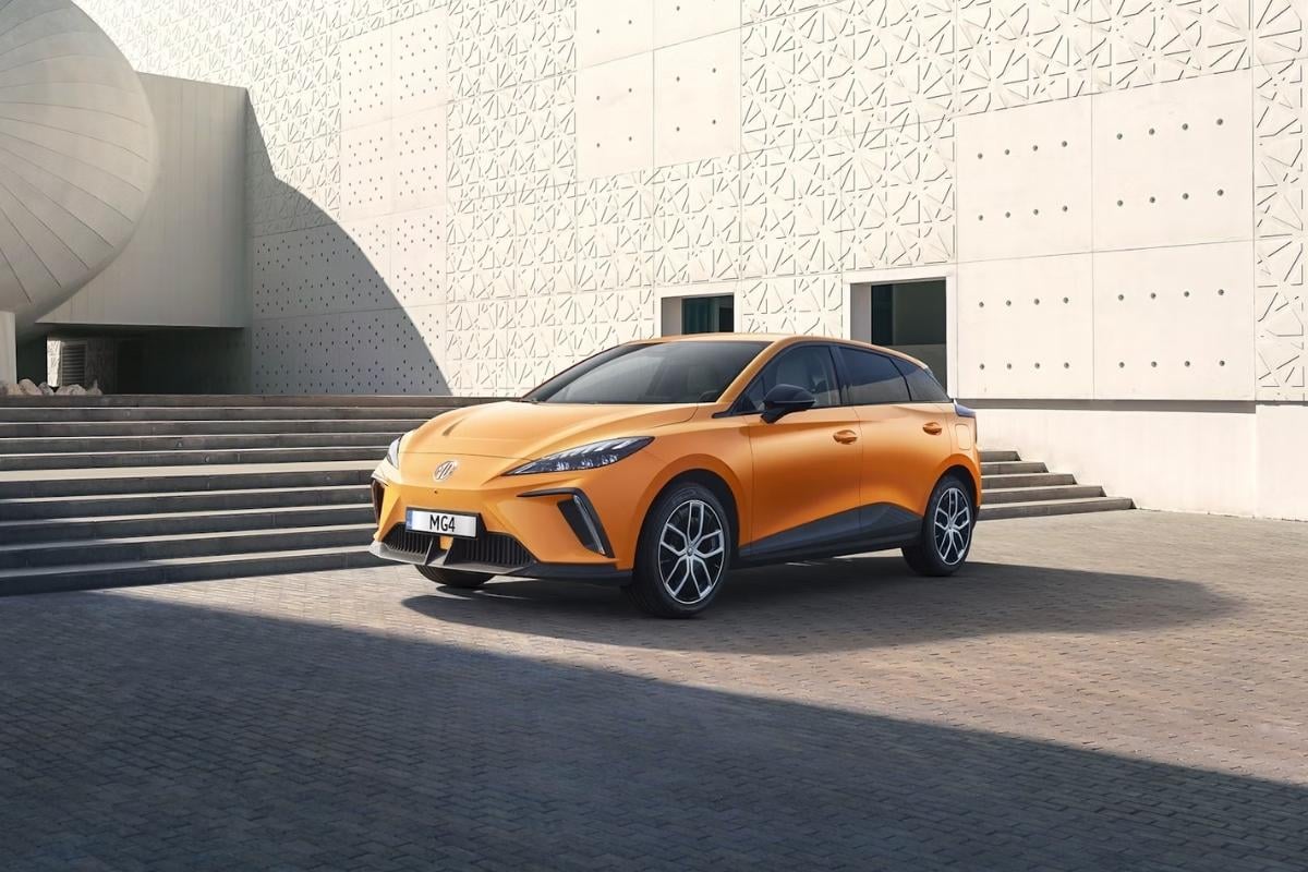 Berline compacte MG4 Electric orange devant un bâtiment moderne, illustrant les nouveaux modèles de voitures électriques récentes qui arrivent sur le marché de l'occasion en 2026