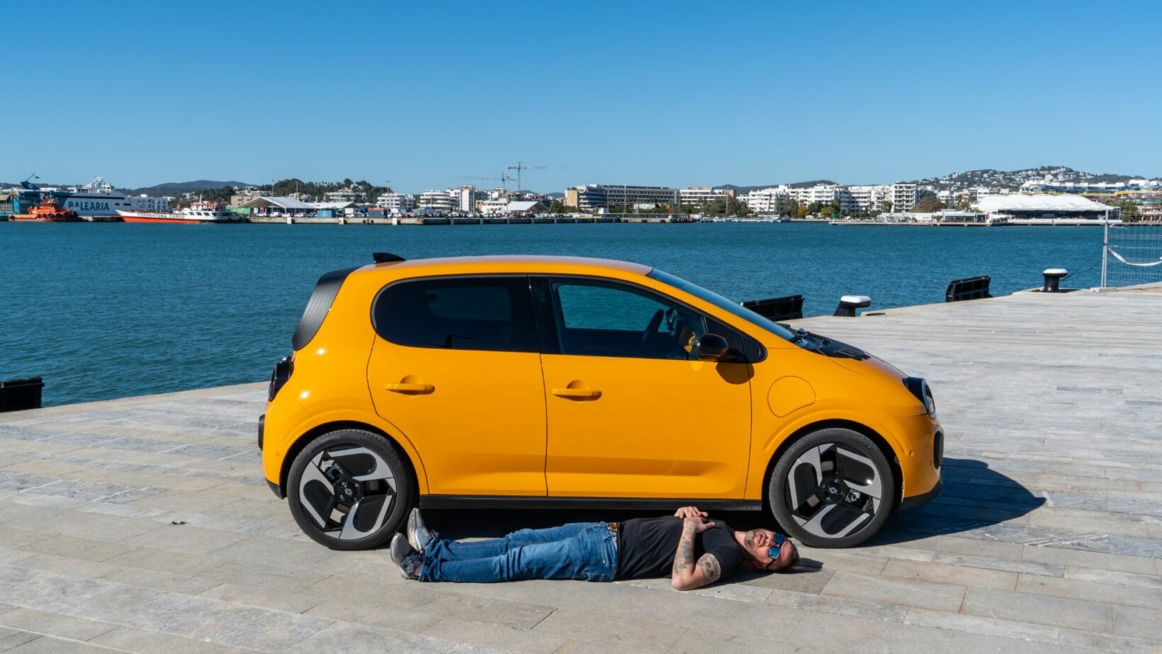 Renault Twingo E-Tech électrique jaune Mango profil avec jantes 18 pouces, homme allongé pour illustrer l’empattement