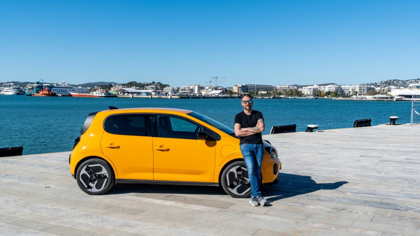 Renault Twingo E-Tech électrique jaune Mango finition Techno avec jantes 18 pouces, essayeur debout devant la voiture