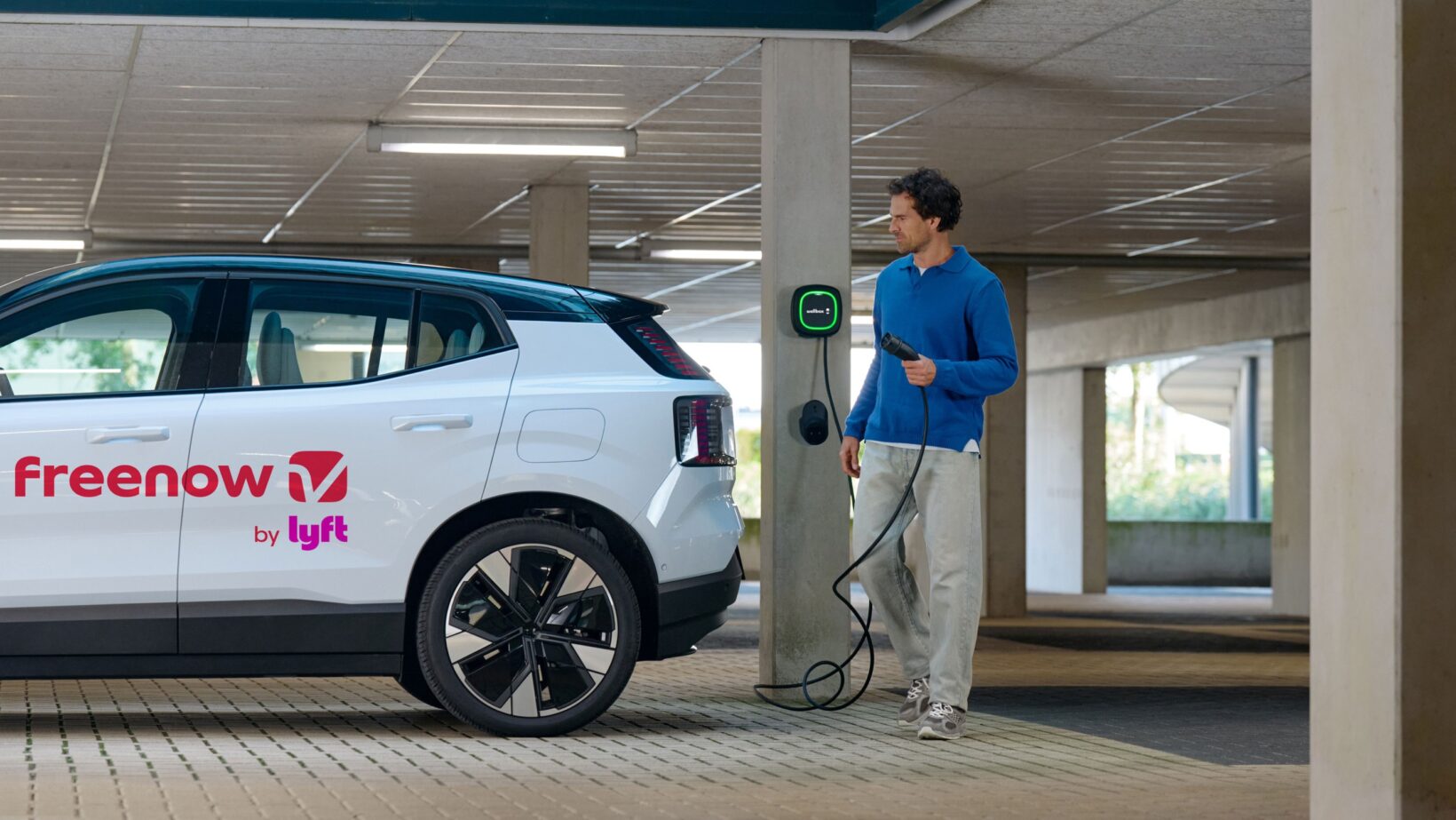 Chauffeur branchant un taxi électrique Volvo EX30 Freenow sur une borne de recharge dans un parking.