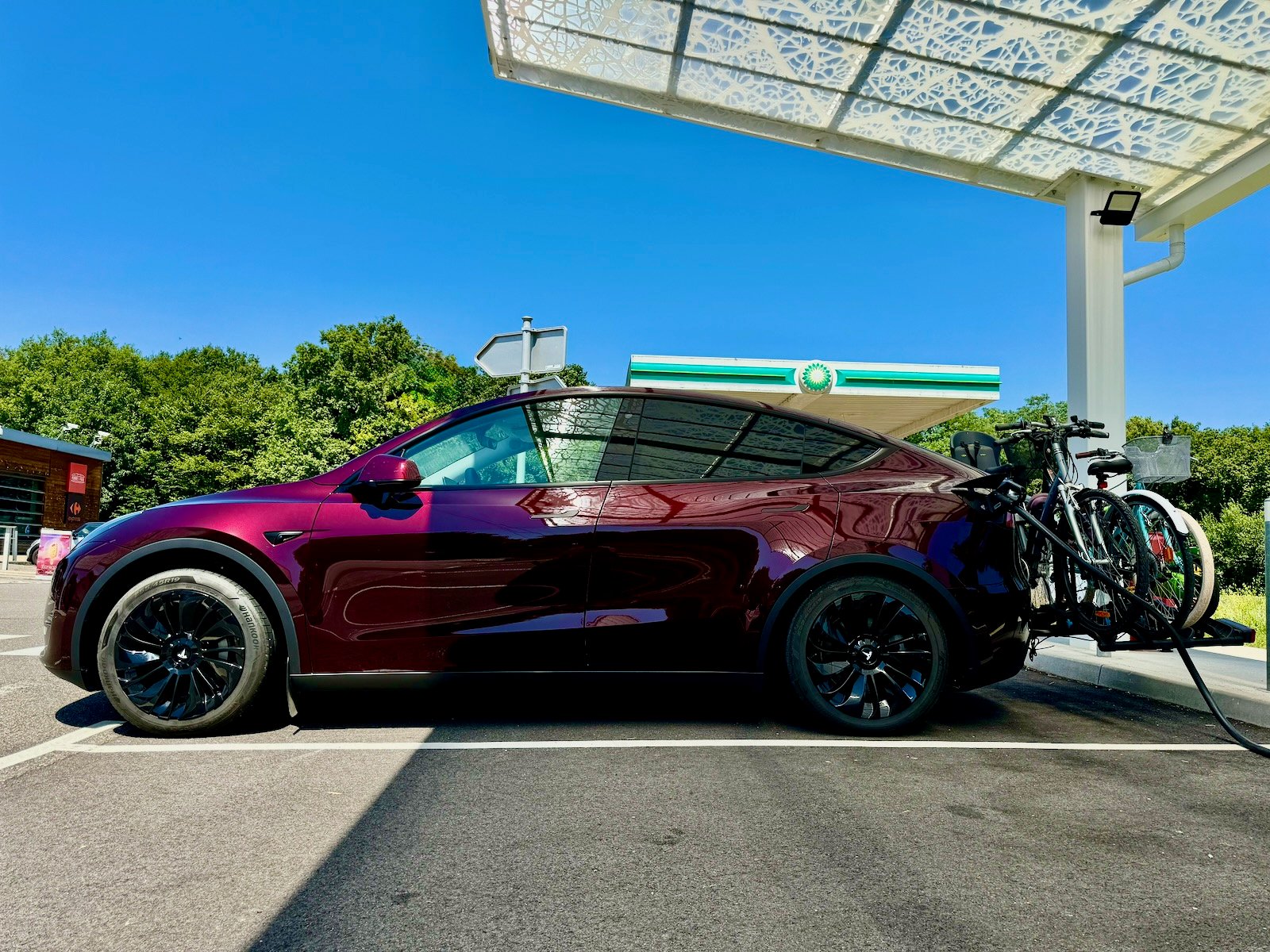 Tesla Model Y rouge équipée de vélos en cours de recharge à une borne sur la route des vacances.