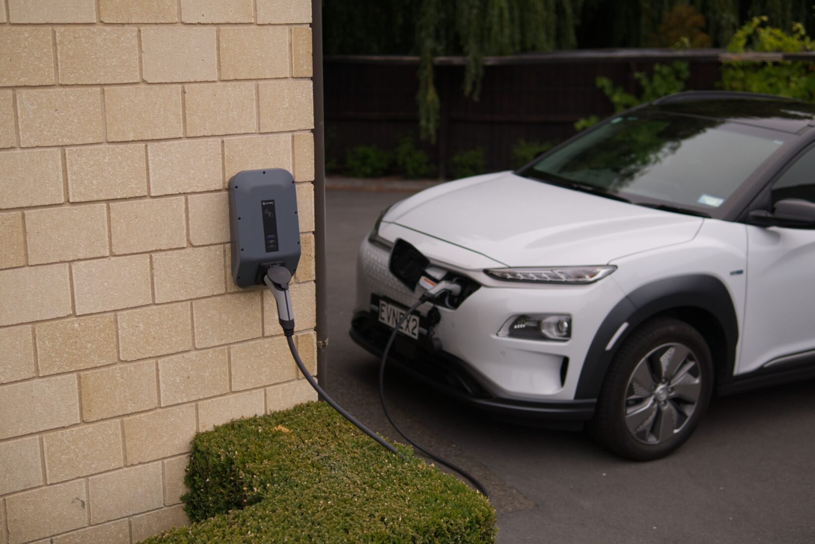Voiture électrique branchée à une wallbox murale devant une maison
