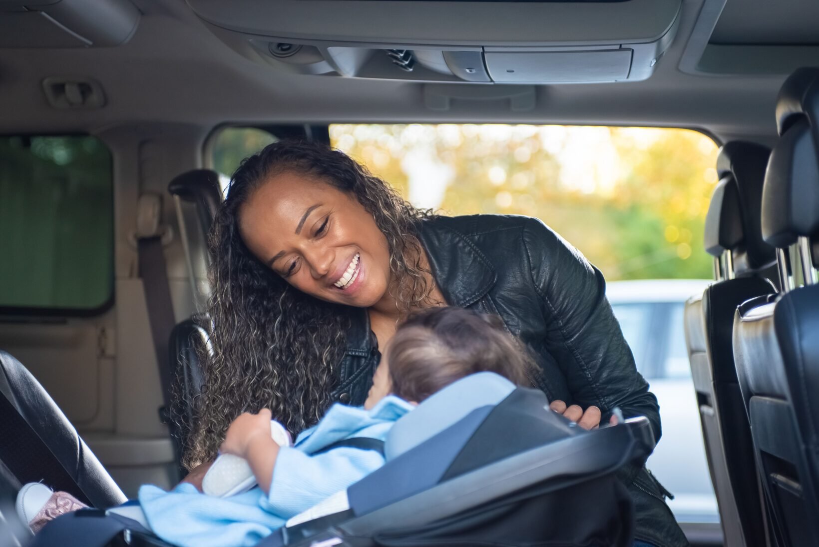 Bébé installé dos à la route dans une coque i-Size, mère souriante penchée vers lui en voiture