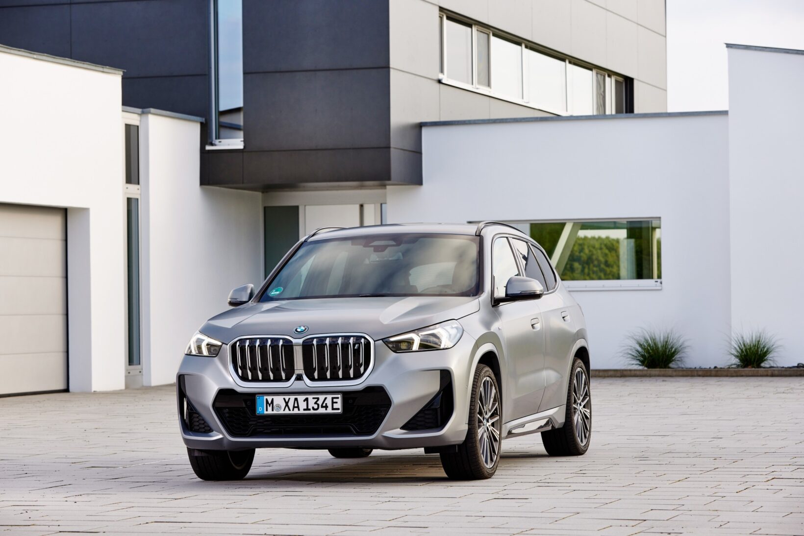 BMW iX1 électrique xDrive30 M Sport gris vu de trois quarts avant devant une maison moderne