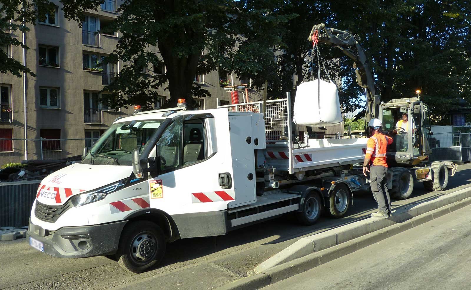 Iveco eDaily électrique de VINCI avec remorque Maxicargo pendant une opération de manutention sur un chantier à Paris.