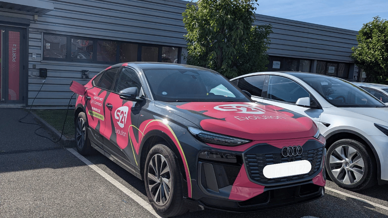 Audi Q6 e-tron rose et grise floquée S2i Evolution branchee a une borne de recharge