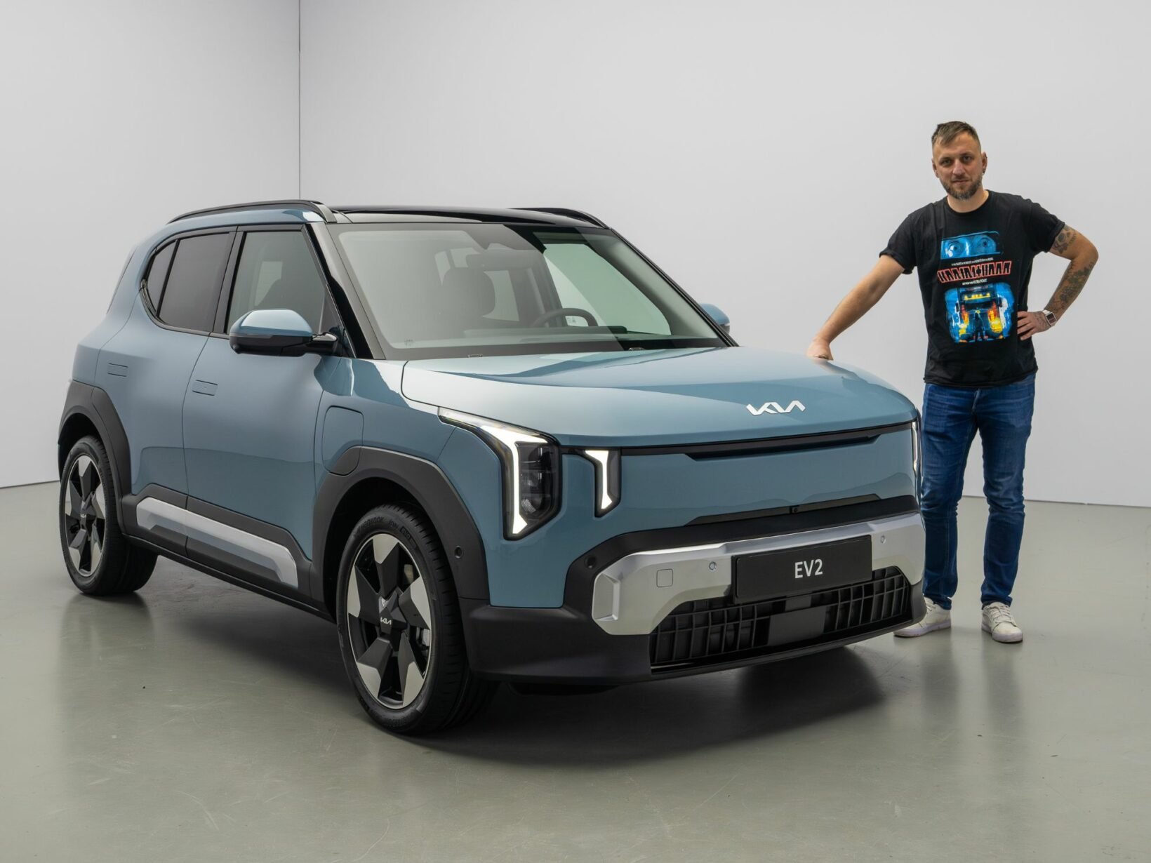 Présentation de la Kia EV2 en studio, vue trois-quarts avant, avec un gabarit adulte pour illustrer les dimensions.