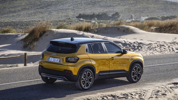 Jeep Avenger électrique jaune vue arrière trois-quarts roulant sur une route près de dunes de sable