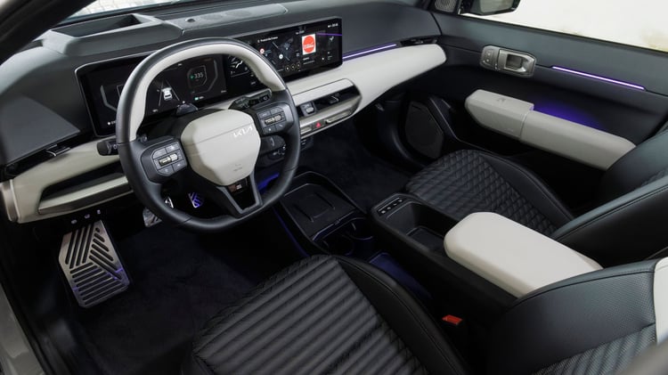 Habitacle avant de la Kia EV4 avec poste de conduite, triple écran panoramique et accoudoir central.