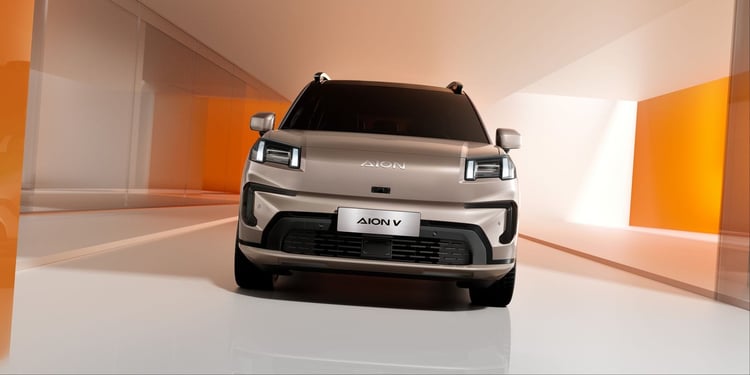 Aion V beige vu de face dans un studio orange, signature lumineuse fine et bouclier noir