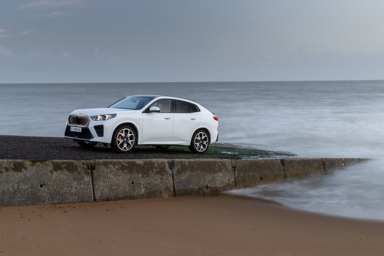BMW iX2 électrique blanche de profil, garée sur une digue en bord de mer