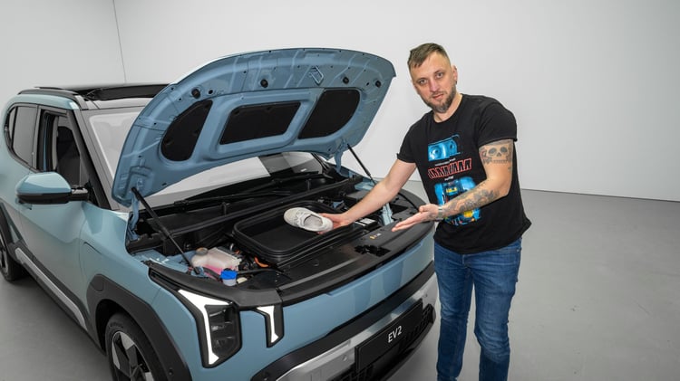 Coffre avant (frunk) de la Kia EV2 avec le capot ouvert, présenté par un homme pour illustrer le rangement.