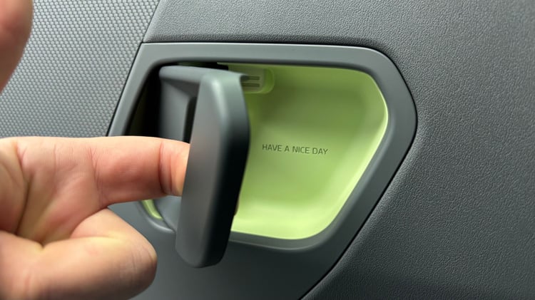 Poignée intérieure de la Kia EV2 : ouverture de porte avec insert vert et message « HAVE A NICE DAY ».