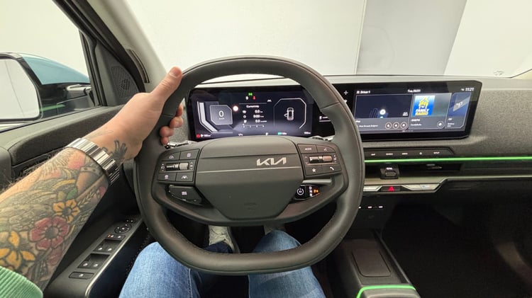 Poste de conduite de la Kia EV2 avec triple écran numérique et bandeau lumineux vert sur la planche de bord.