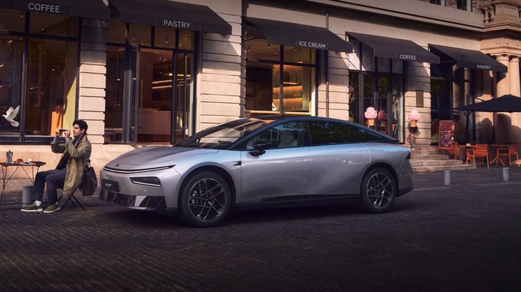 Berline électrique XPeng P7+ grise garée en ville devant des boutiques, vue trois-quarts avant