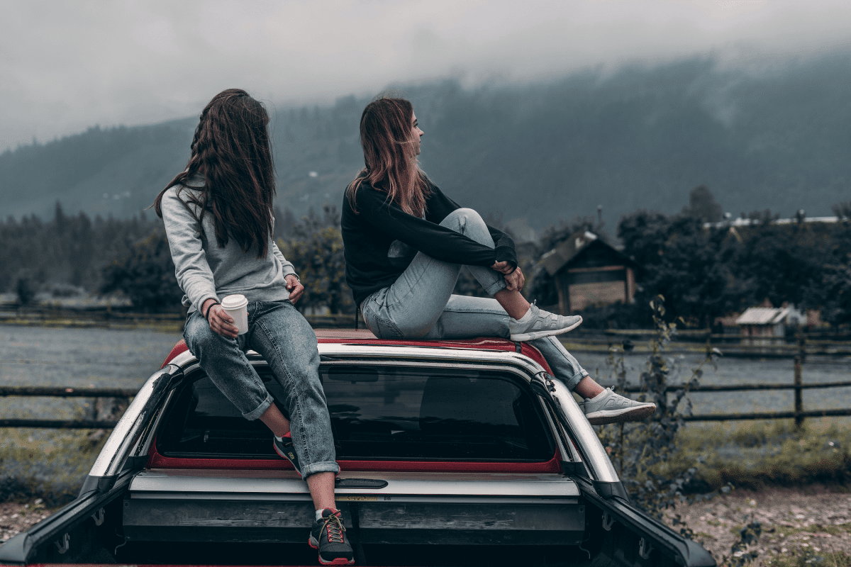 Deux jeunes femmes sur le toit d'une voiture contemplant un paysage montagneux
