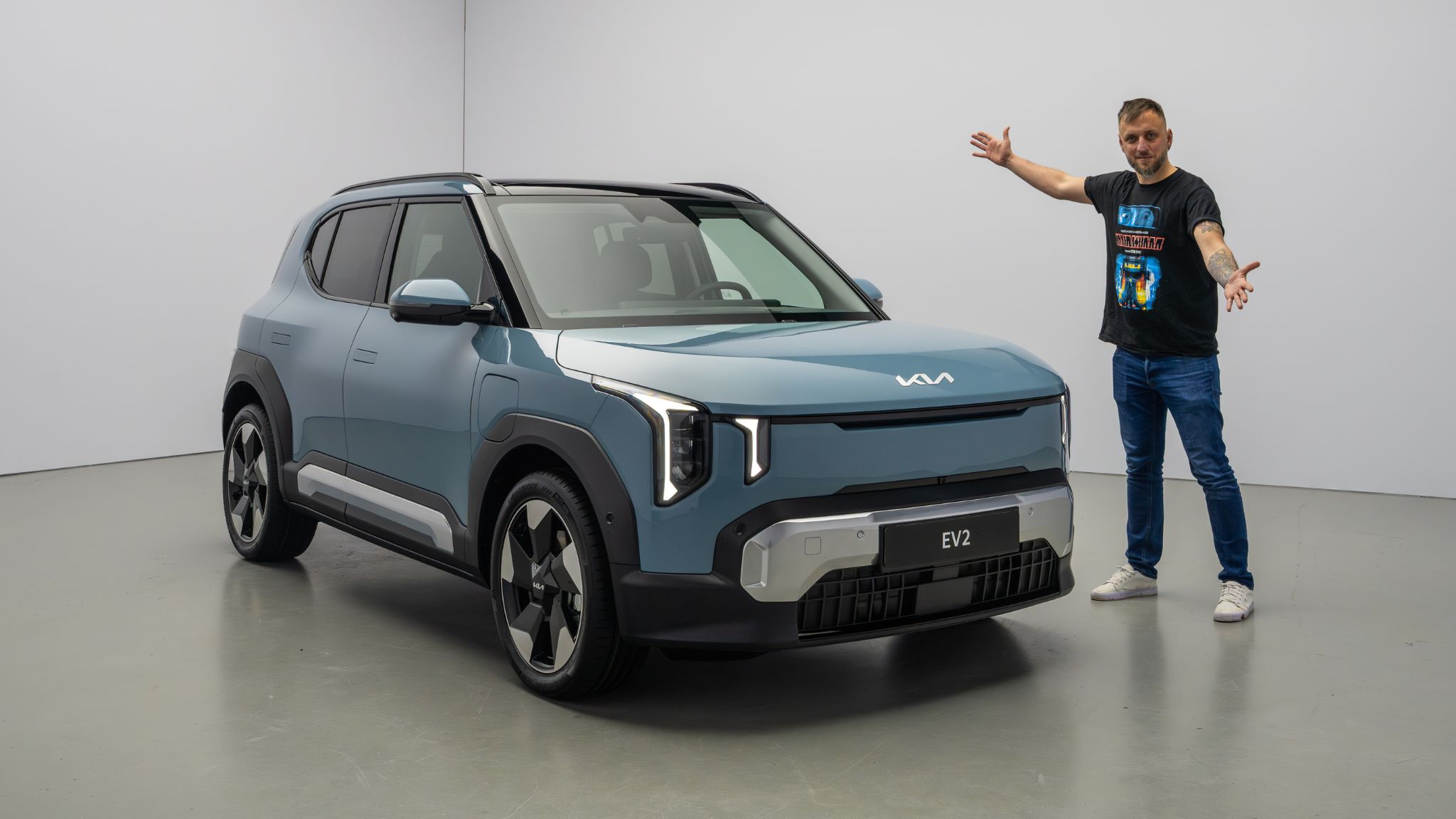 Kia EV2 bleu, vue trois-quarts avant avec personne debout à côté.